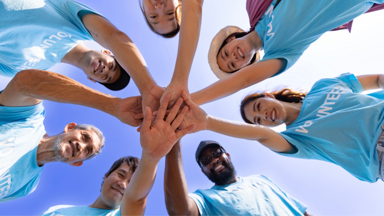 Groupe de bénévoles formant un cercle, les bras devant et les mains réunies au centre