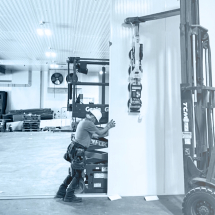 Travailleur positionnant un panneau isolant pour chambre froide à l'aide d’un chariot élévateur, en noir et blanc