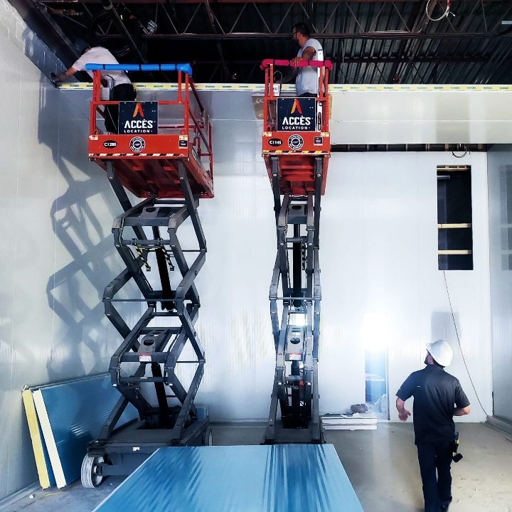 Travailleurs en nacelle installant le plafond dans une chambre froide en construction