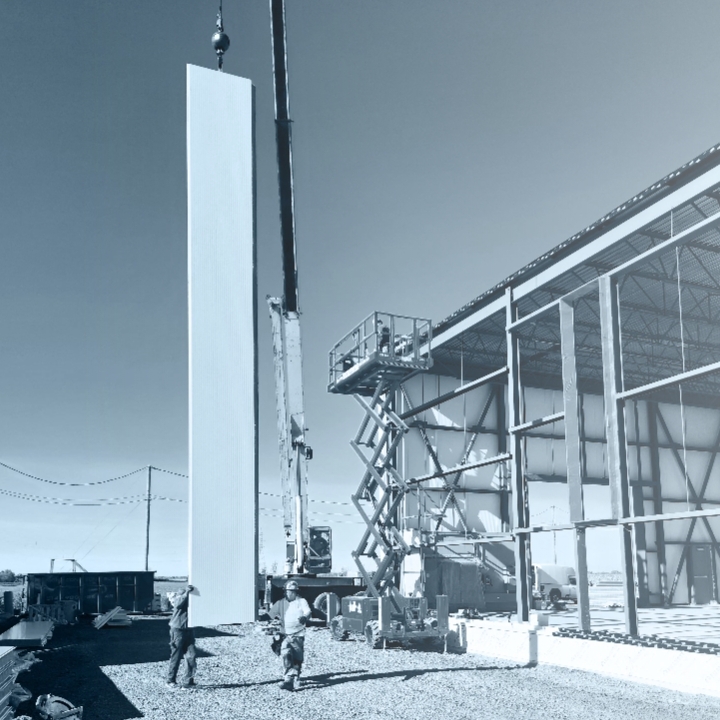 Installation d’un panneau isolant mural sur un bâtiment industriel à l’aide d’une nacelle et d’une grue, en noir et blanc