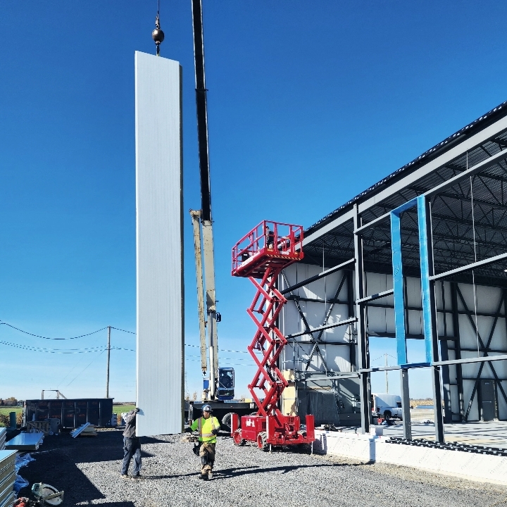 Installation d’un panneau isolant mural sur un bâtiment industriel à l’aide d’une nacelle et d’une grue