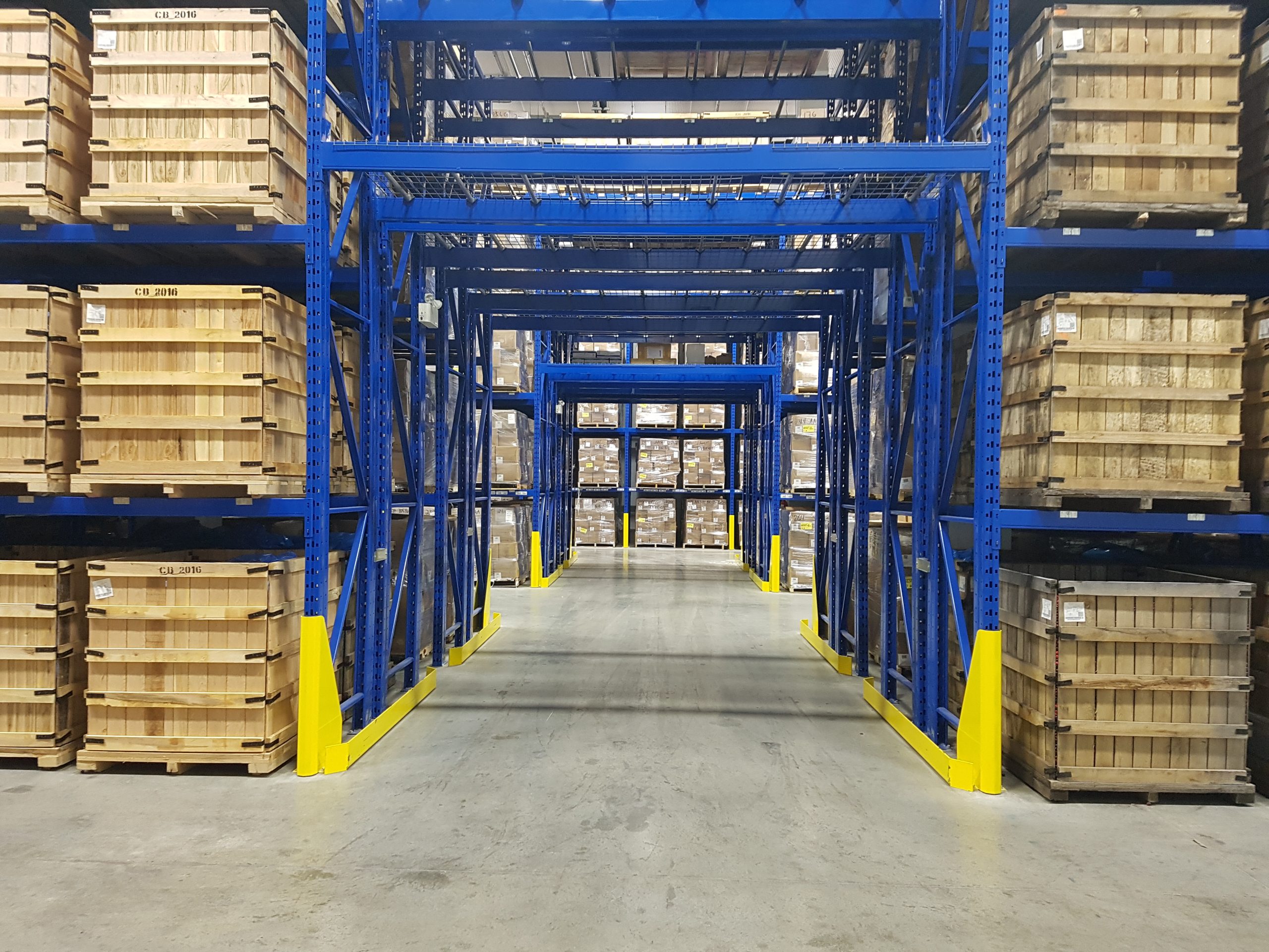 Allée centrale d’un entrepôt industriel avec rayonnage métallique bleu et palettes de bois entreposées
