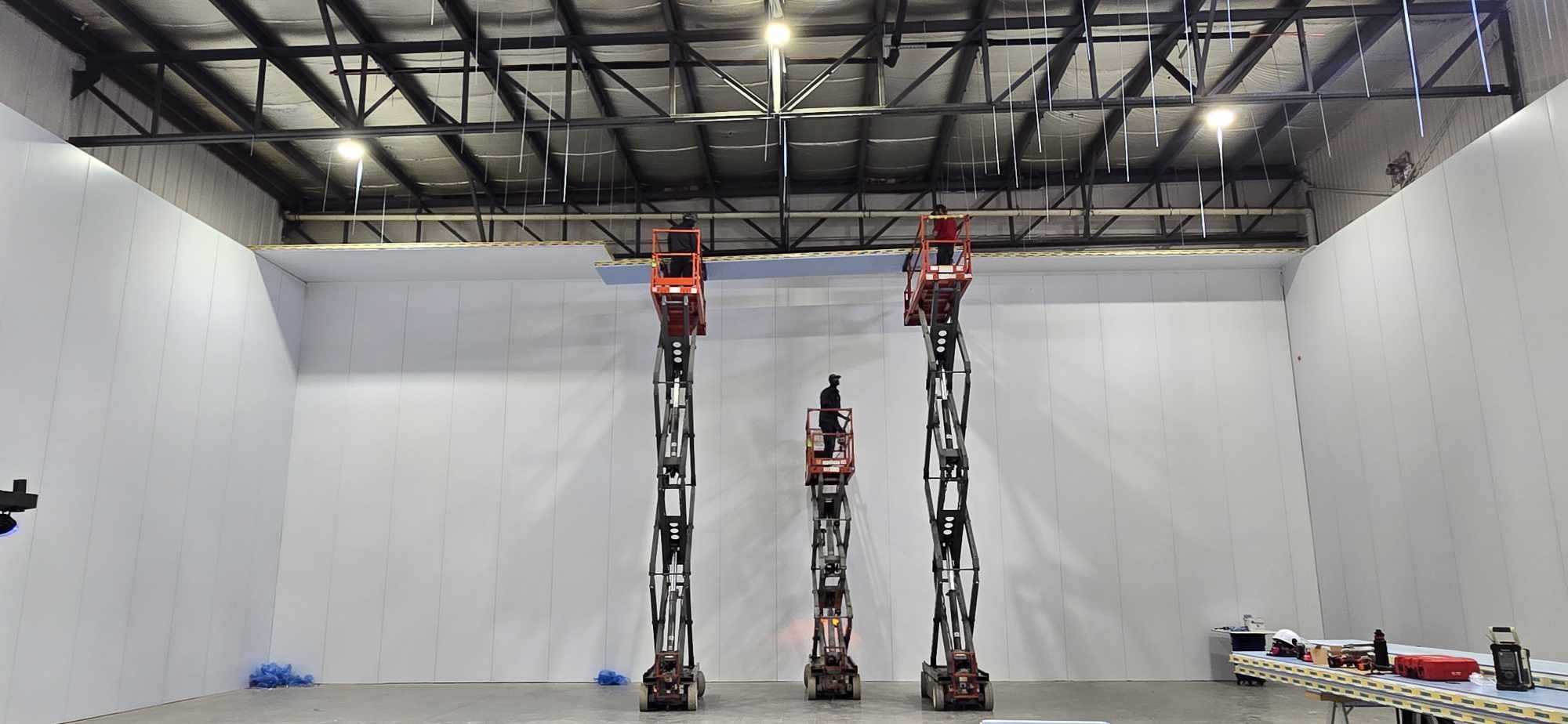 Travailleurs sur nacelles effectuant l'installation du plafond d’une chambre froide de grande hauteur