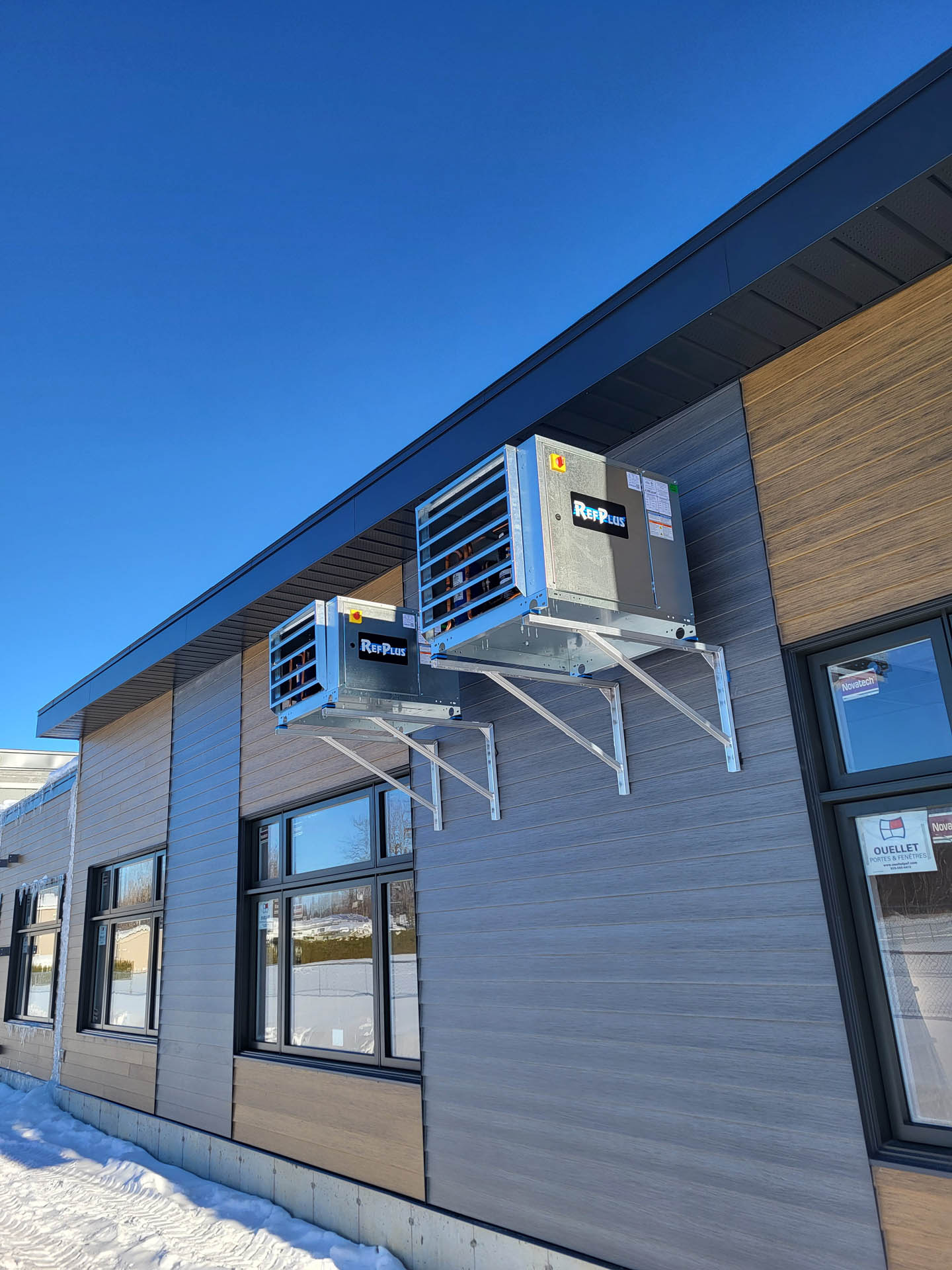 Deux unités de réfrigération murales installées sur la façade extérieure d’un bâtiment commercial en hiver.