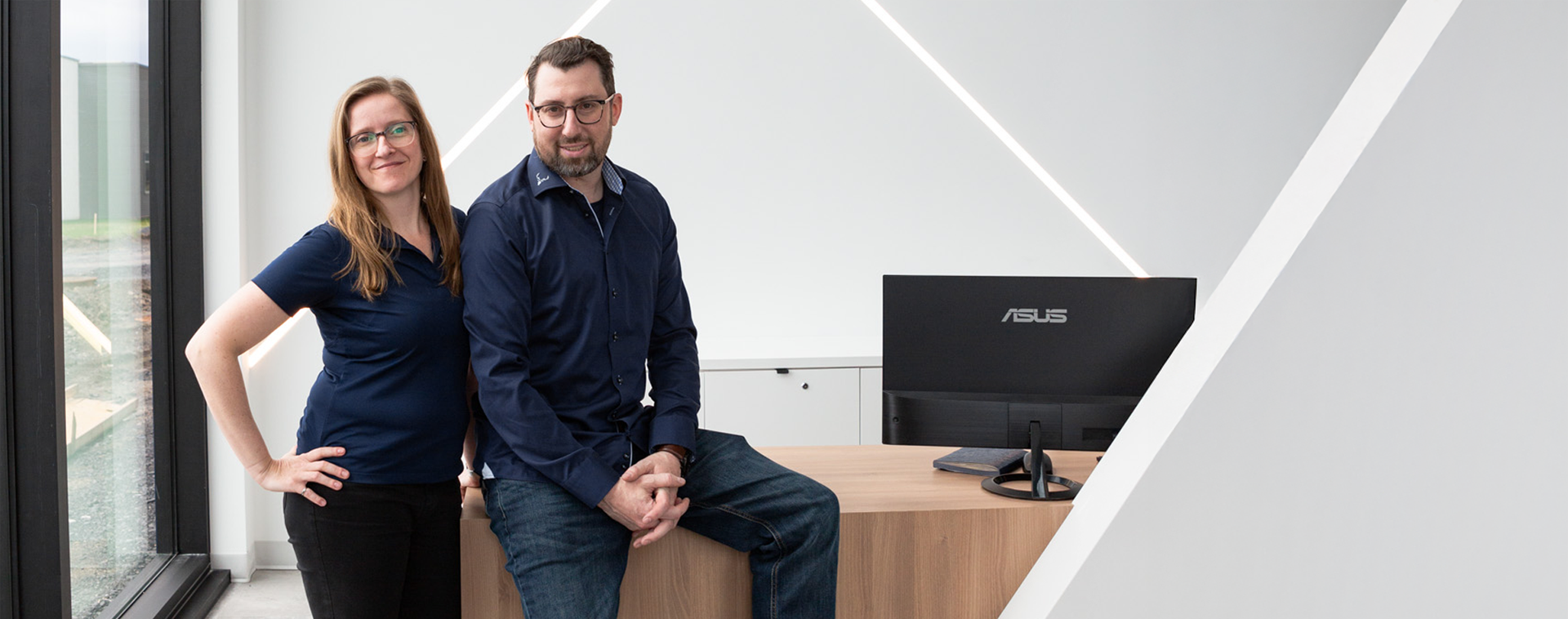 Deux collègues souriants dans un bureau, dont un assis sur le comptoir en bois